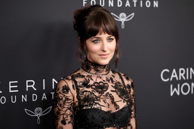 Dakota memilih riasan wajah minimalis bernuansa nude dengan fokus pada eyeshadow bergaya smokey. Rambut brunette-nya disanggul tinggi, menyisakan poni dan beberapa helaian rambut yang membingkai wajah. Foto: Getty Images/Mike Coppola
