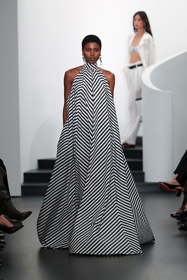 Warna utama untuk jaket dan mantel adalah putih bersih, seperti pada busana pertama: mantel polo putih panjang yang terbuka memperlihatkan bra hitam dipadukan dengan celana hitam. (Foto: Dia Dipasupil/Getty Images)