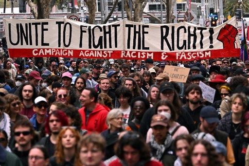 People hold up placards during an anti-racism protest march in Melbourne on September 13, 2025 to counter anti-immigration and anti-government protesters from a Save Australia rally. (Photo by William WEST / AFP)
