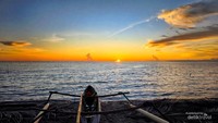Perahu nelayan tradisional di pantai dengan siluet matahari terbenam yang memukau