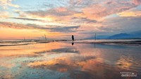 Seorang nelayan memantulkan langit senja di air dangkal dengan pemandangan gunung di kejauhan