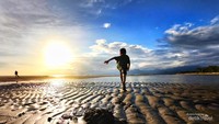 Anak laki laki berlarian di pasir pantai meninggalkan jejak kaki