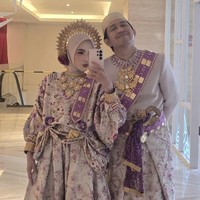 Diketahui busana adat yang dikenakan Feby dan Adam berasal dari Enj Project. Detail busana berupa kain bernuansa floral ungu-krem dengan aksen emas, serta selempang ungu berhias ornamen keemasan membuat penampilan keduanya terlihat memukau. Foto: Instagram/@fbyputrinc