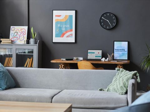 Wide shot of cozy flat interior with home office area including big sofa, wooden table and motivational posters at dark-gray wall