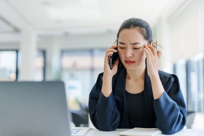 Young Asian businesswoman having a headache and massaging her temples while making a phone call in the office