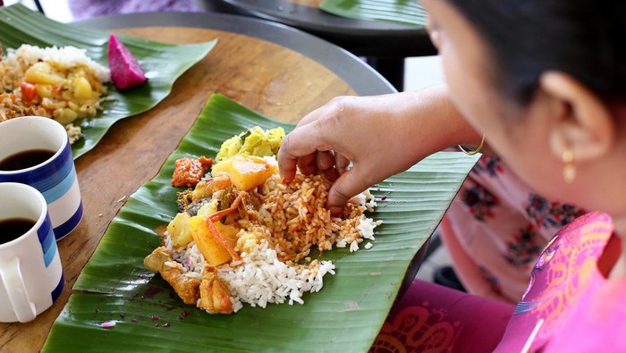 An Asian woman is enjoying banana leaf rice during lunch potluck session.