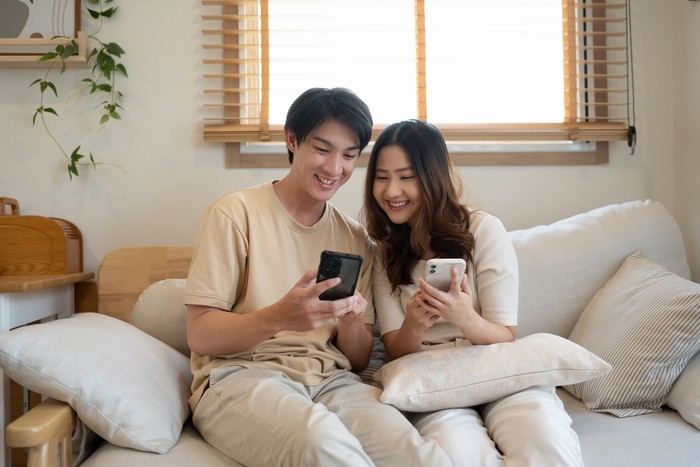Young couple enjoying weekend time together with their smartphones on sofa at home.