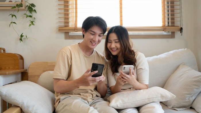 Young couple enjoying weekend time together with their smartphones on sofa at home.