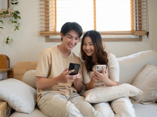 Young couple enjoying weekend time together with their smartphones on sofa at home.