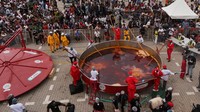 Asisten membantu mengaduk campuran nasi jollof dalam panci raksasa sambil uap panas mengepul keluar. Foto: REUTERS/Sodiq Adelakun