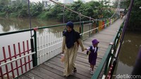Warga melintasi jembatan gantung di atas Banjir Kanal Barat, Tanah Abang, Jakarta Pusat.
