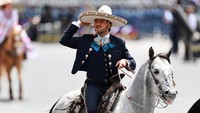Seorang pria berpakaian seperti charro tampak gagah saat membawa bendera Meksiko di tengah parade. REUTERS/Raquel Cunha