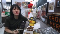 Kulineran Ria SW di Pasar Bintaro berlanjut ke gerai pisang goreng. Ia menikmati pisang goreng madu yang disajikan dengan gula aren bubuk. Foto: YouTube/Ria SW