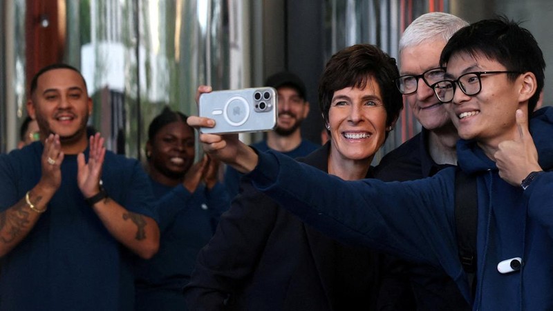 Apple CEO Tim Cook and Deirdre O'Brien, senior vice president of retail and people at Apple Inc., take a picture with a customer, as the iPhone 17 series goes on sale, at the Apple Store in New York City, U.S., September 19, 2025. REUTERS/Shannon Stapleton