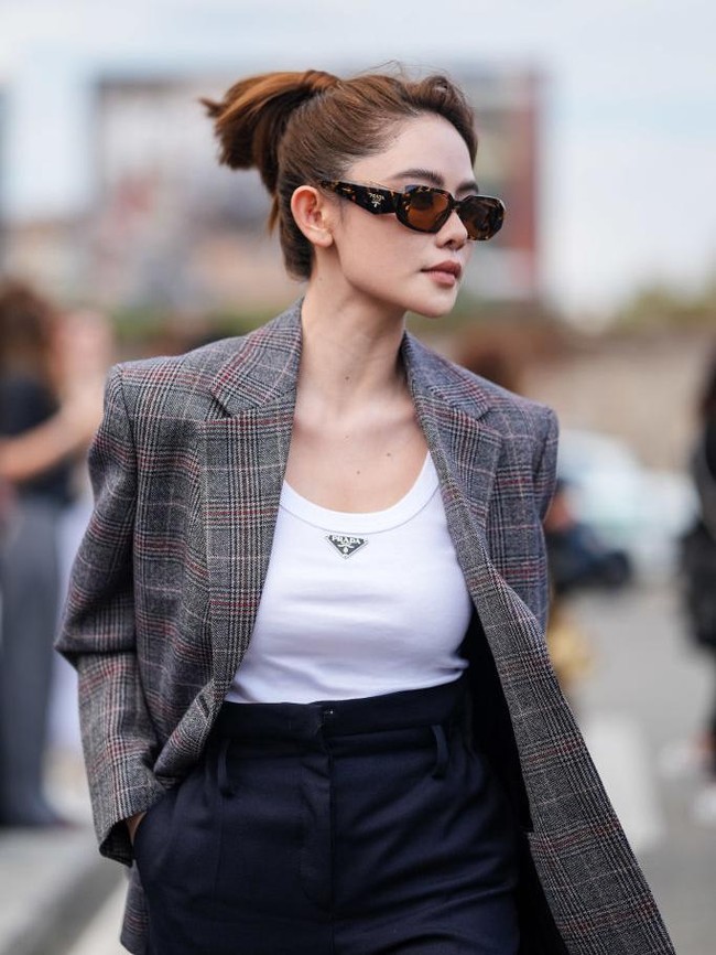 Doudou Babe mengenakan kacamata hitam Prada, tank top Prada putih, jaket blazer oversized bermotif abu-abu tua, dan tas kulit Prada abu-abu muda, di luar Prada, selama Milan Fashion Week Musim Semi/Panas 2024-2025 pada 19 September 2024 di Milan, Italia.