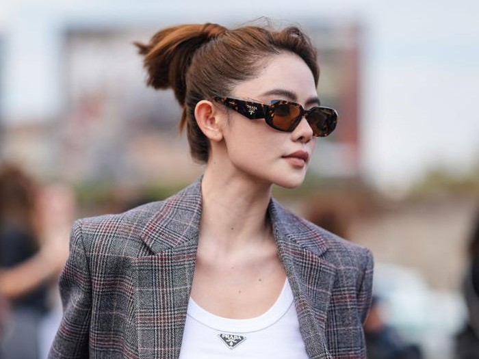 Doudou Babe mengenakan kacamata hitam Prada, tank top Prada putih, jaket blazer oversized bermotif abu-abu tua, dan tas kulit Prada abu-abu muda, di luar Prada, selama Milan Fashion Week Musim Semi/Panas 2024-2025 pada 19 September 2024 di Milan, Italia.