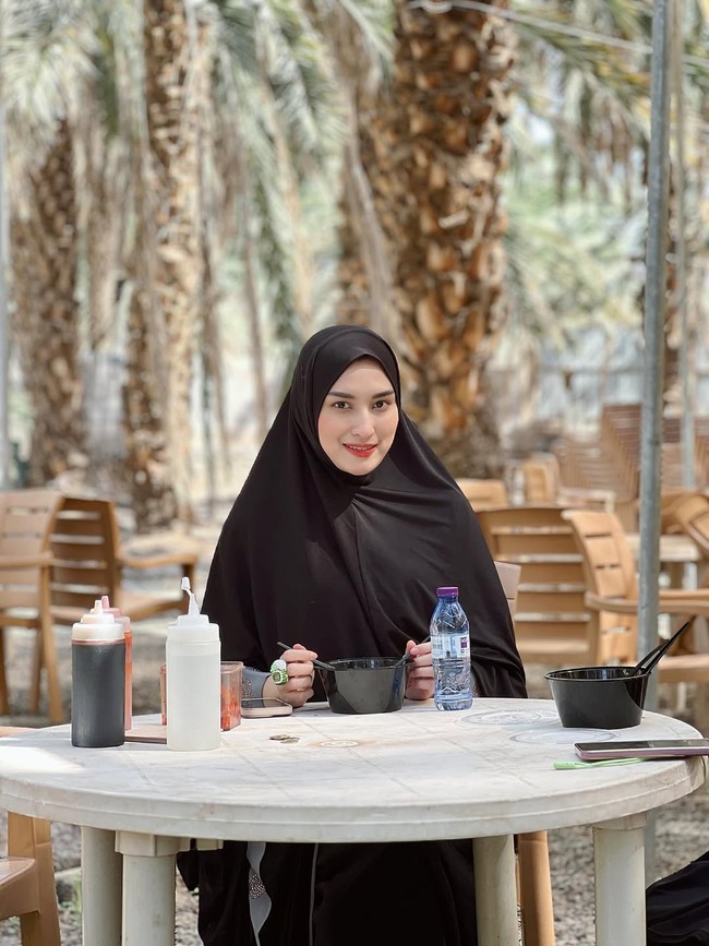 Angbeen Rishi menikmati santapan sederhana di kebun kurma, tetap tampil natural dengan hijab hitam polos. Foto: Dok. Instagram/@angbeenrishi.
