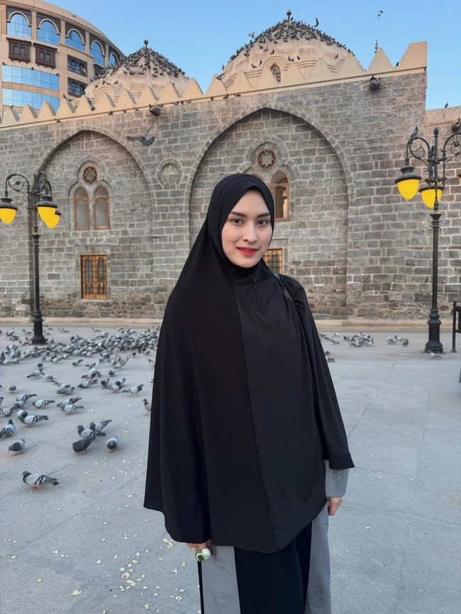Dengan latar Masjid Ghamamah di Madinah dan kawanan burung merpati, Angbeen terlihat menawan dalam hijab syari hitam polos yang menonjolkan sisi anggun. Foto: Dok. Instagram/@angbeenrishi.