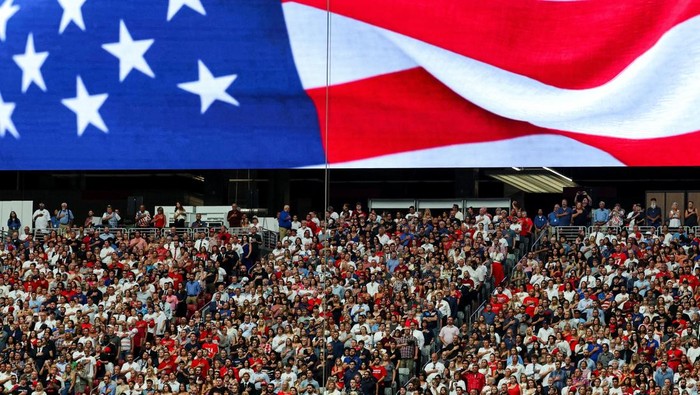Lautan Pelayat Penuhi Arizona Peringati Kepergian Charlie Kirk A large screen displays an image of a U.S. flag, as people stand for the national anthem, during the memorial service for slain conservative commentator Charlie Kirk at State Farm Stadium, in Glendale, Arizona, U.S., September 21, 2025. REUTERS/Daniel Cole