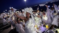 Peserta Diner en Blanc berpakaian putih berkumpul di Robert F. Wagner Jr. Park, New York, menghadirkan suasana elegan di bawah langit Manhattan. Diner en Blanc adalah pesta makan malam bergaya Prancis yang sangat unik, pertama kali digelar di Paris pada tahun 1988. Foto: REUTERS/Jeenah Moon