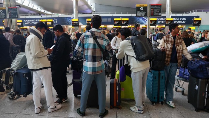 A man uses a smartphone as travellers queue to check in at Heathrow Airport Terminal 4, following a disruption to check-in and boarding systems caused by a cyber attack which has affected several major European airports, resulting in flight delays and cancellations, in Greater London, Britain, September 20, 2025. REUTERS/Isabel Infantes
