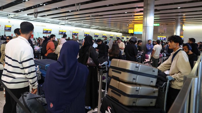 A man uses a smartphone as travellers queue to check in at Heathrow Airport Terminal 4, following a disruption to check-in and boarding systems caused by a cyber attack which has affected several major European airports, resulting in flight delays and cancellations, in Greater London, Britain, September 20, 2025. REUTERS/Isabel Infantes