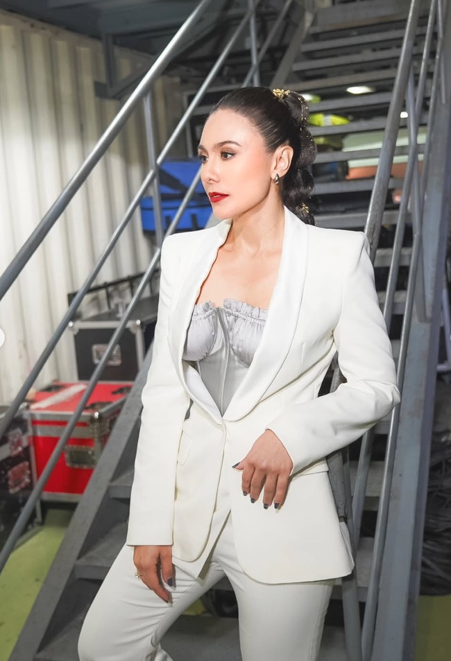 Wulan tampil dalam setelan blazer putih yang dipadukan dengan bustier satin abu-abu sebagai inner, memberi kesan seksi namun tetap classy. Look Wulan paling menonjolkan aura glamor. Paduan blazer putih dengan bustier abu-abu, ponytail unik, dan lipstik merah menghadirkan gaya sophisticated dan berani. Foto: Instagram/@wulanguritno/@masayuanastasia