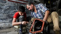 Di sebuah bengkel kecil di Baghdad, Irak, seorang anak laki-laki tampak tekun membantu ayahnya memperbaiki girboks mobil. Tangannya yang masih kecil harus kotor oleh oli, sementara teman sebayanya di tempat lain mungkin sedang bermain bebas. REUTERS/Ahmed Saad