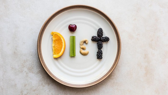 The word Diet made from food. A orange slice, celery stick, cherry, cashew, and blackberry spell diet, as it sits on a stoneware plate. Using a flat lay over head view to capture the spelled out food word.