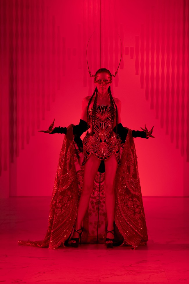 Perempuan 38 tahun itu tampil mengenakan bustier artistik dengan detail sulaman rumit bernuansa keemasan, dipadukan dengan jubah berpayet yang menjuntai megah. Aksesori berupa topeng ornamentik dan struktur kepala menyerupai antena menambah kesan teatrikal, membuat penampilannya bak karakter villain dalam film fantasi futuristik. (Foto: Dok. Senayan City)