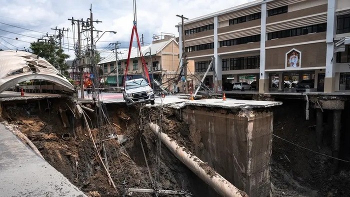 A vehicle is removed from the edge of a hole in the ground after a road collapsed near a hospital in Bangkok on September 24, 2025. A portion of a busy road in the Thai capital caved in early on September 24, leaving a massive 50-metre-deep hole in front of a main hospital and forcing people nearby to evacuate. (AFP)
