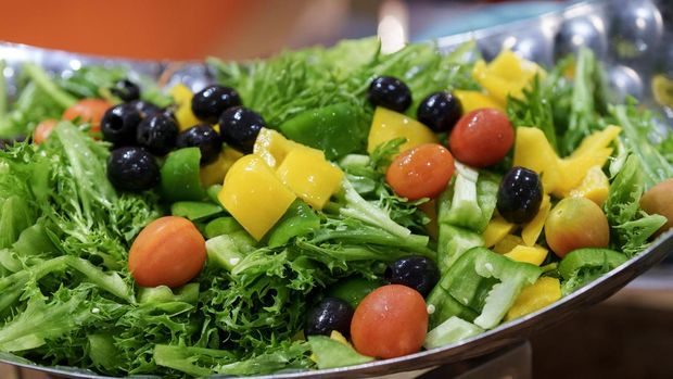 A vibrant bowl of fresh mixed salad with cherry tomatoes, bell peppers, black olives, and lettuce, served in a buffet setting.