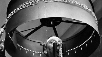 Foto tahun 1960 ini mengabadikan sebuah eksperimen aneh di RAF Institute of Aviation Medicine. Dr. G. H. Byford terlihat mengenakan lensa kontak yang dilengkapi lampu mini sambil berdiri di bawah drum optokinetik yang berputar. Foto: Harry Thompson/Getty Images via Bored Panda
