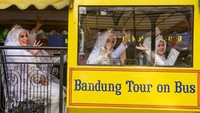 Para pengantin melambaikan tangan saat menaiki bus Bandros usai akad nikah gratis di Bandung, Jumat (26/9/2025). Momen ini menjadi simbol perayaan kebahagiaan pasangan yang baru saja diresmikan. ANTARA FOTO/Novrian Arbi