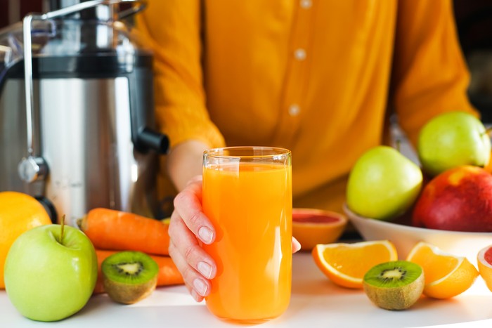 A womans hand holds a glass of freshly made natural multifruit juice. Healthy and tasty juices at home. Using a juicer. Close-up. Selective focus.