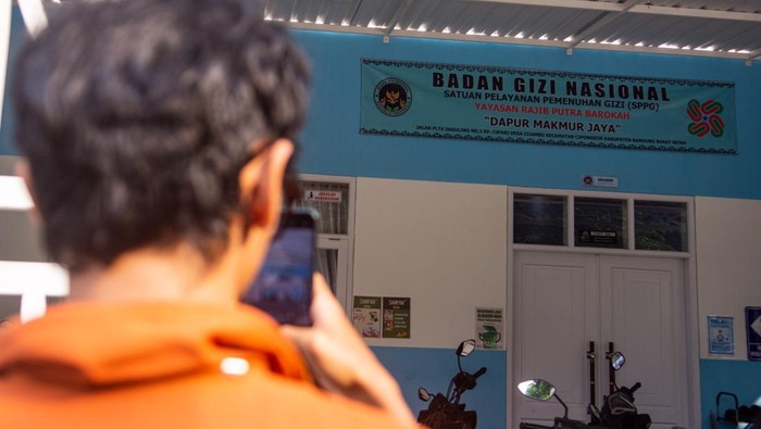 Jurnalis melintas di depan kendaraan pengantar makan bergizi gratis (MBG) di fasilitas Satuan Pelayanan Pemenuhan Gizi  dapur Makmur Jaya di Cipongkor, Kabupaten Bandung Barat, Jawa Barat, Jumat (26/9/2025). Pemerintah Kabupaten Bandung Barat menutup sementara tiga dapur penyedia makanan program Makan Bergizi Gratis (MBG) yang diduga menjadi penyebab keracunan massal siswa di Kecamatan Cipongkor hingga keluarnya hasil uji laboratorium dan evaluasi dari Badan Gizi Nasional (BGN). ANTARA FOTO/Novrian Arbi/rwa.