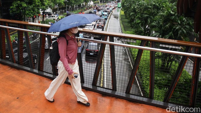 Warga menembus gerimis di JPO Pinisi Jl Jendral Sudirman, Jakarta, Senin (29/9/2025).