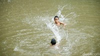 Air kecoklatan Kalimalang tak menyurutkan keceriaan anak-anak yang tetap bermain di tengah derasnya hujan.