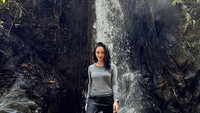 Gaya Ririn berfoto dengan aliran air terjun di belakangnya.
