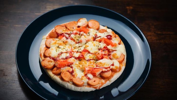 Pizza, sausage and crab sticks in a ceramic plate on a wooden table.