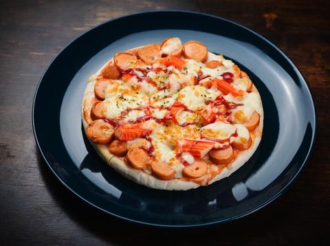 Pizza, sausage and crab sticks in a ceramic plate on a wooden table.