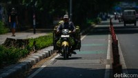 Seorang pengendara motor tanpa helm terlihat melawan arah di jalur sepeda. Penggunaan jalur khusus ini melanggar aturan dan membahayakan pengguna jalan.