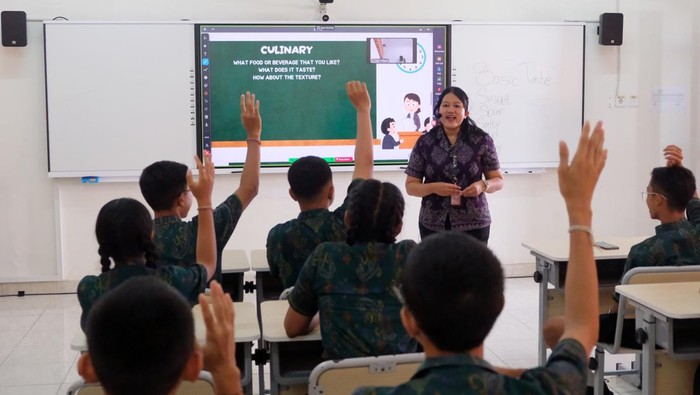 Seorang guru memberikan penjelasan kepada siswa yang mengikuti pelajaran bahasa inggris dengan metode pembelajaran smart classroom atau ruang kelas pintar di SMP Negeri 15 Denpasar, Bali, Jumat (3/10/2025). Kegiatan tersebut merupakan bagian dari peluncuran teknologi Wi-Fi 7 dengan kecepatan hingga 2 Gbps sekaligus penerapan smart classroom atau ruang kelas pintar yakni metode pembelajaran modern yang mengintegrasikan teknologi digital dan konektivitas internet serta dapat melakukan kolaborasi belajar virtual antar sekolah. ANTARA FOTO/Nyoman Hendra Wibowo/YU