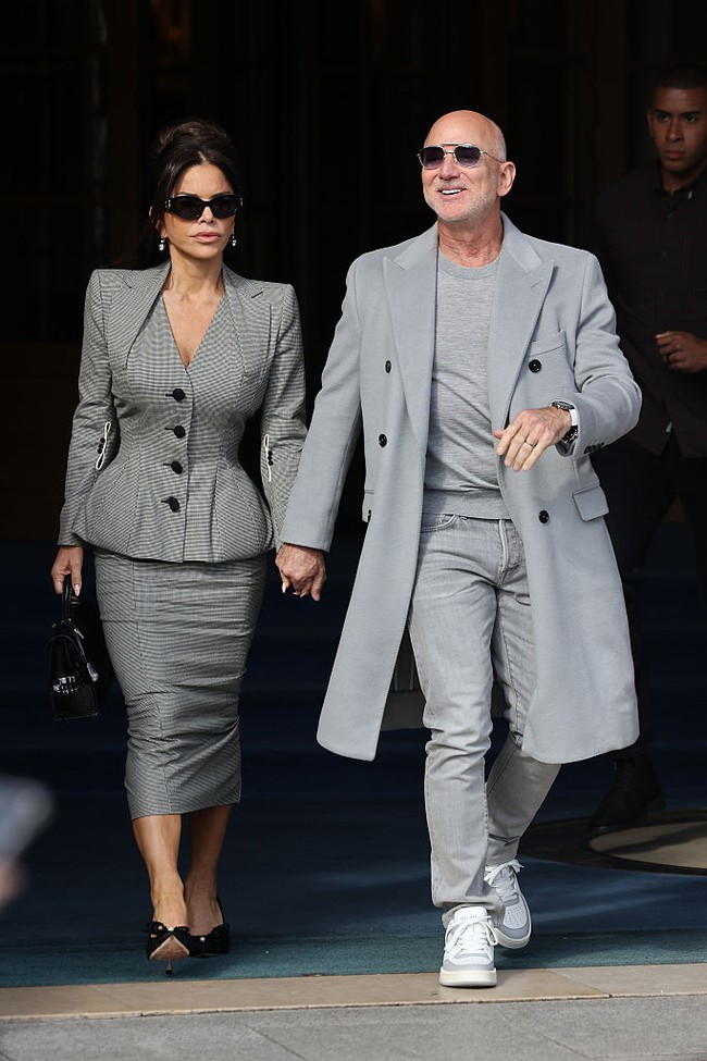 Pendiri Amazon itu tampil dengan kaus dan jeans yang dipadukan dengan coat abu-abu serta sneakers. Sedangkan Lauren Sanchez mengenakan setelan kotak-kotak vintage karya John Galliano tahun 1995. Setelan itu terdiri dari blazer peplum dan rok pensil. Foto: Getty Images/Neil Mockford