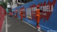 Petugas PPSU menyelesaikan detail mural bertema “Membuka Jendela dan Pintu Tiap Hari”. Ajakan sederhana ini mengingatkan pentingnya sirkulasi udara bagi kesehatan rumah.