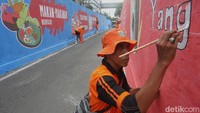 Petugas PPSU melukis mural bertema hidup sehat di dinding gang Cikoko, Pancoran, Jakarta Selatan, Selasa (7/10/2025). Kampanye ini mengajak warga menjaga kebersihan lingkungan dan kesehatan diri.