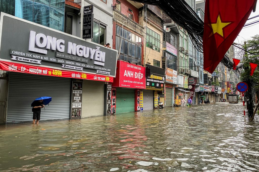 Orang-orang berjalan melalui jalan yang banjir di tengah hujan lebat akibat Topan Matmo, yang menyebabkan kendaraan terlantar, menutup sekolah, memindahkan kelas daring, dan menunda penerbangan ke dan dari Bandara Internasional Noi Bai, di Hanoi, Vietnam, 7 Oktober 2025. (REUTERS/Thinh Tien Nguyen)