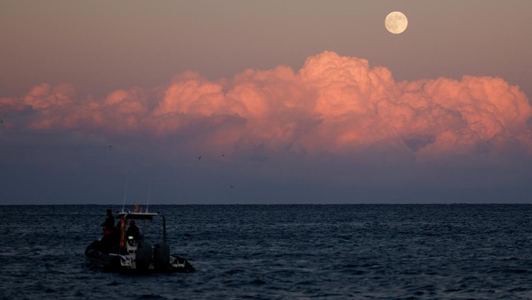 Divers stand on a RHIB (a rigid inflatable boat) as the full moon, known as the Harvest Moon, and also the first supermoon of the year, rises after sunset off Mellieha, Malta, October 6, 2025. REUTERS/Darrin Zammit Lupi