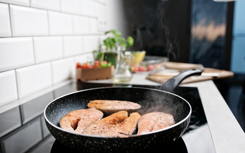 Red Fish Salmon Frying And Steaming In A Pan On The Kitchen Stove