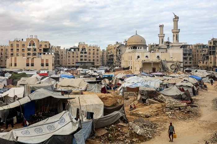 A man carries a jerrycan as he walks past tents sheltering people displaced by war pitched near the heavily-damaged Sheikh Hamad bin Khalifa Al-Thani mosque at the Qatari-built Hamad City residential complex in northwestern Khan Yunis, in the southern Gaza Strip, on October 6, 2025. Delegations from Hamas, Israel and the United States are holding talks in Egypt on October 6, with President Donald Trump urging negotiators to 